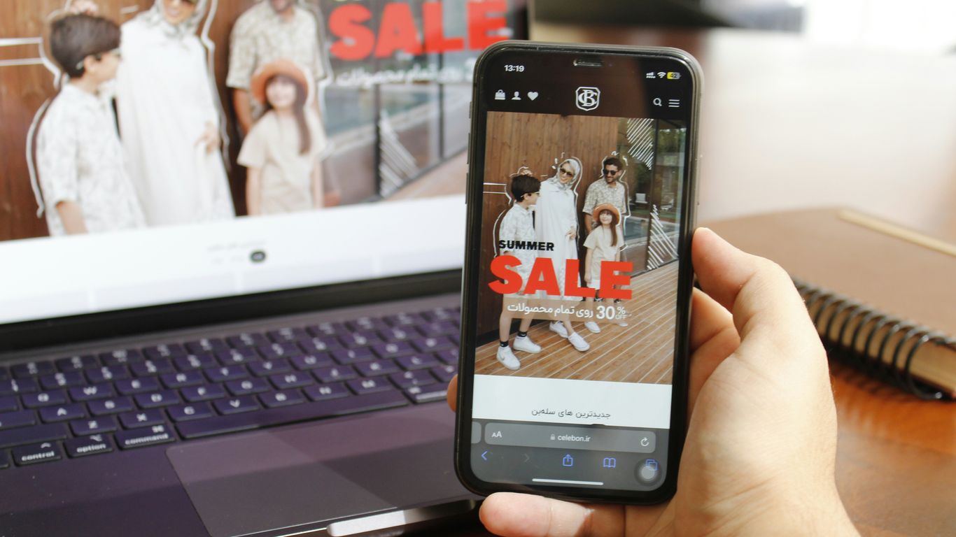A person holding a cell phone in front of a laptop