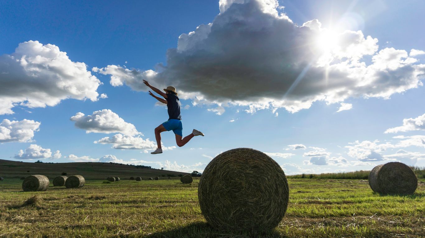 A person jumps in a field with hay bales