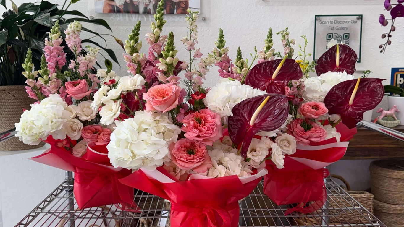 Three floral arrangements with pink and white flowers in red wrapping.