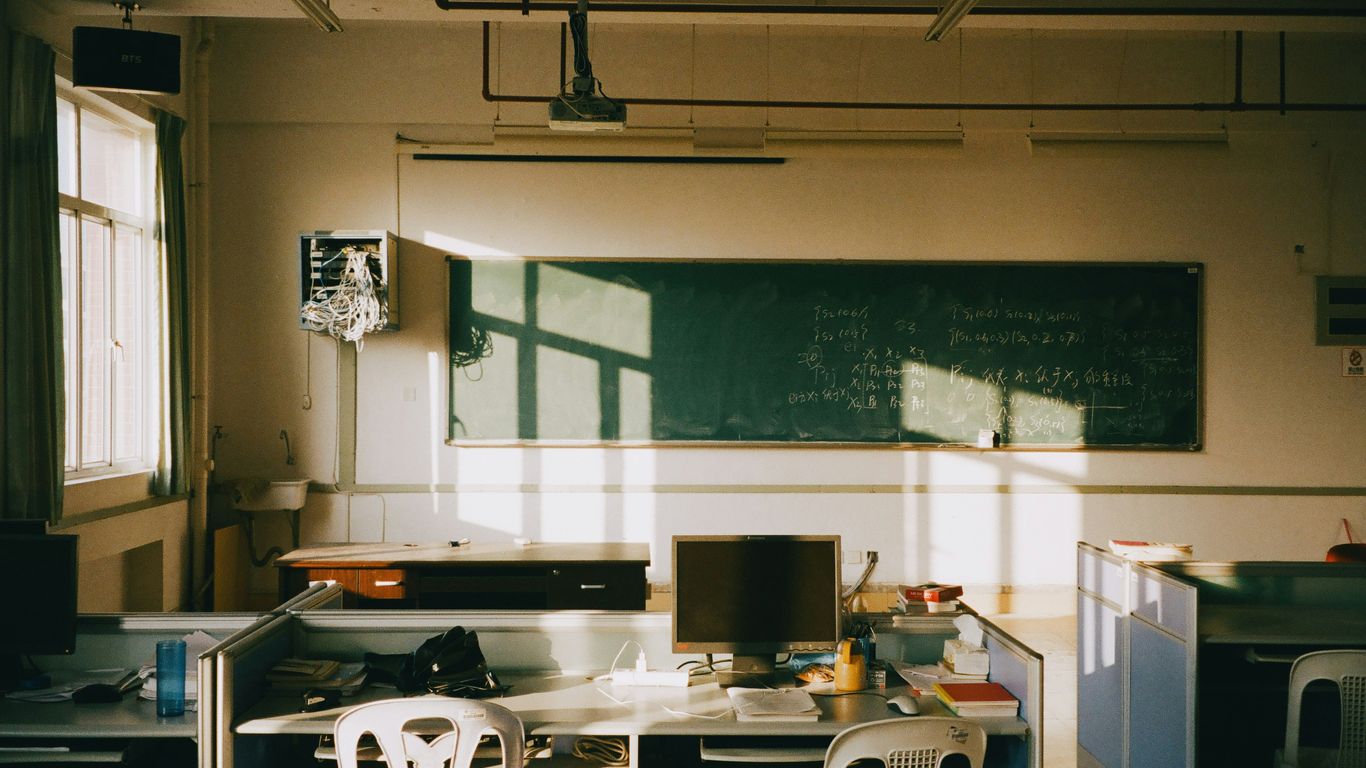 Sunlight streams into an empty classroom with desks.