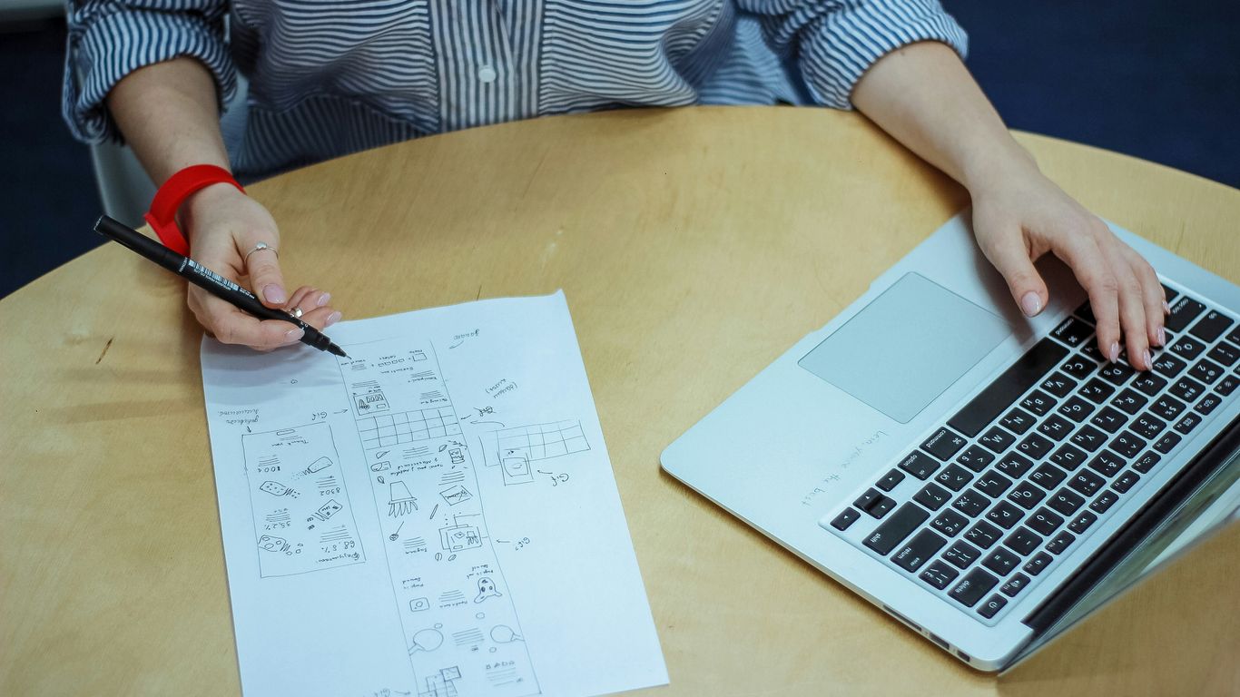 woman sketch on piece of paper while using laptop