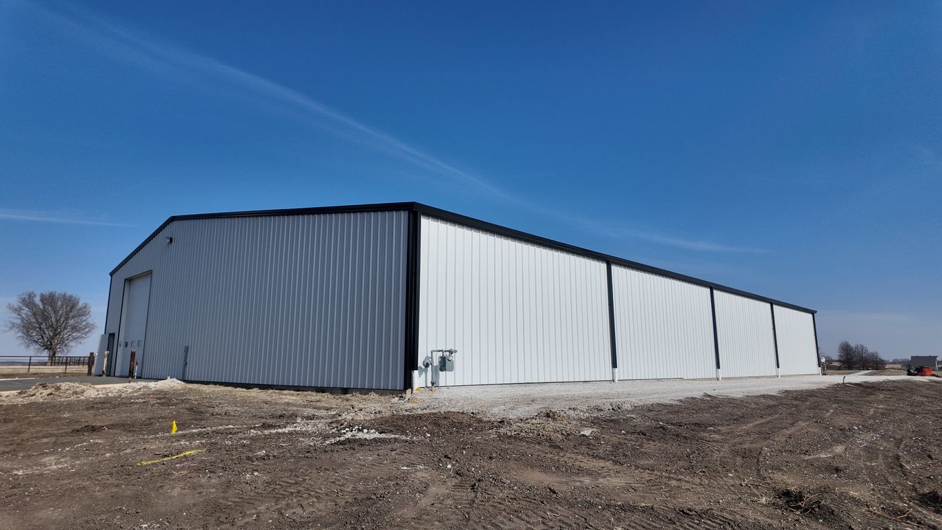 A large, white, corrugated metal building under a clear blue sky.