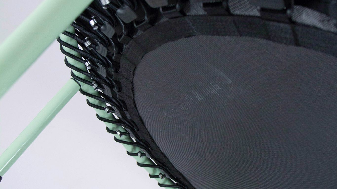 Close-up of a mini trampoline with green frame and cords.