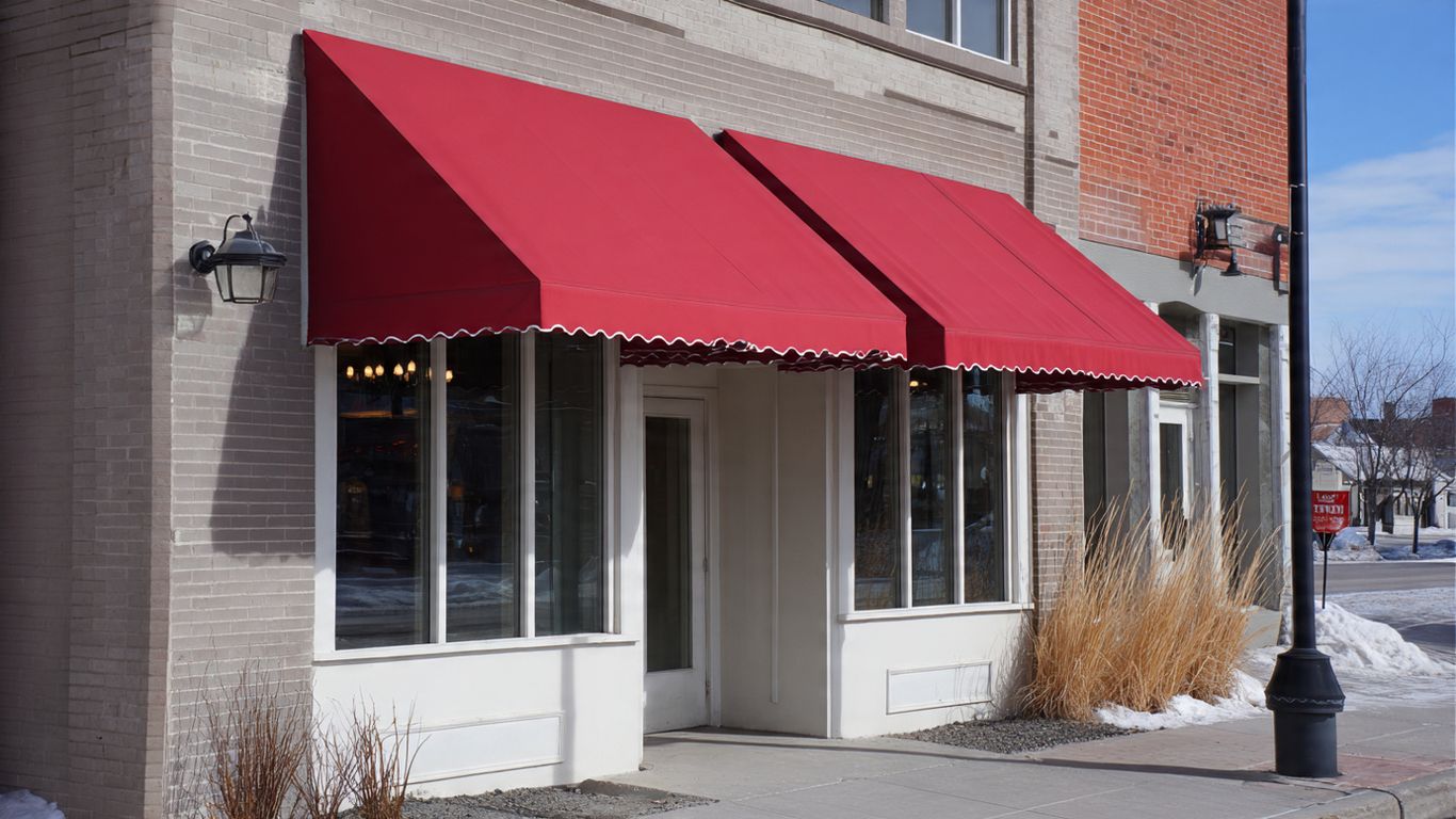 A storefront with red awnings and large windows on a sunny day.