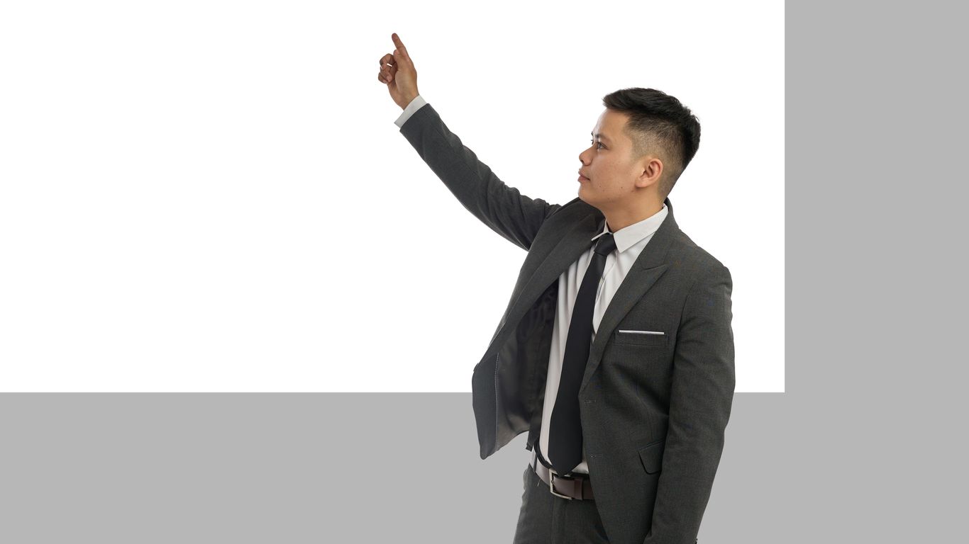A businessman points upward at a blank screen.