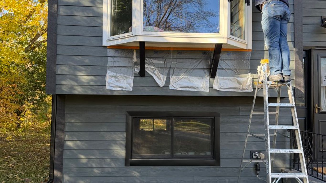 Person on ladder working on a bay window on a house.