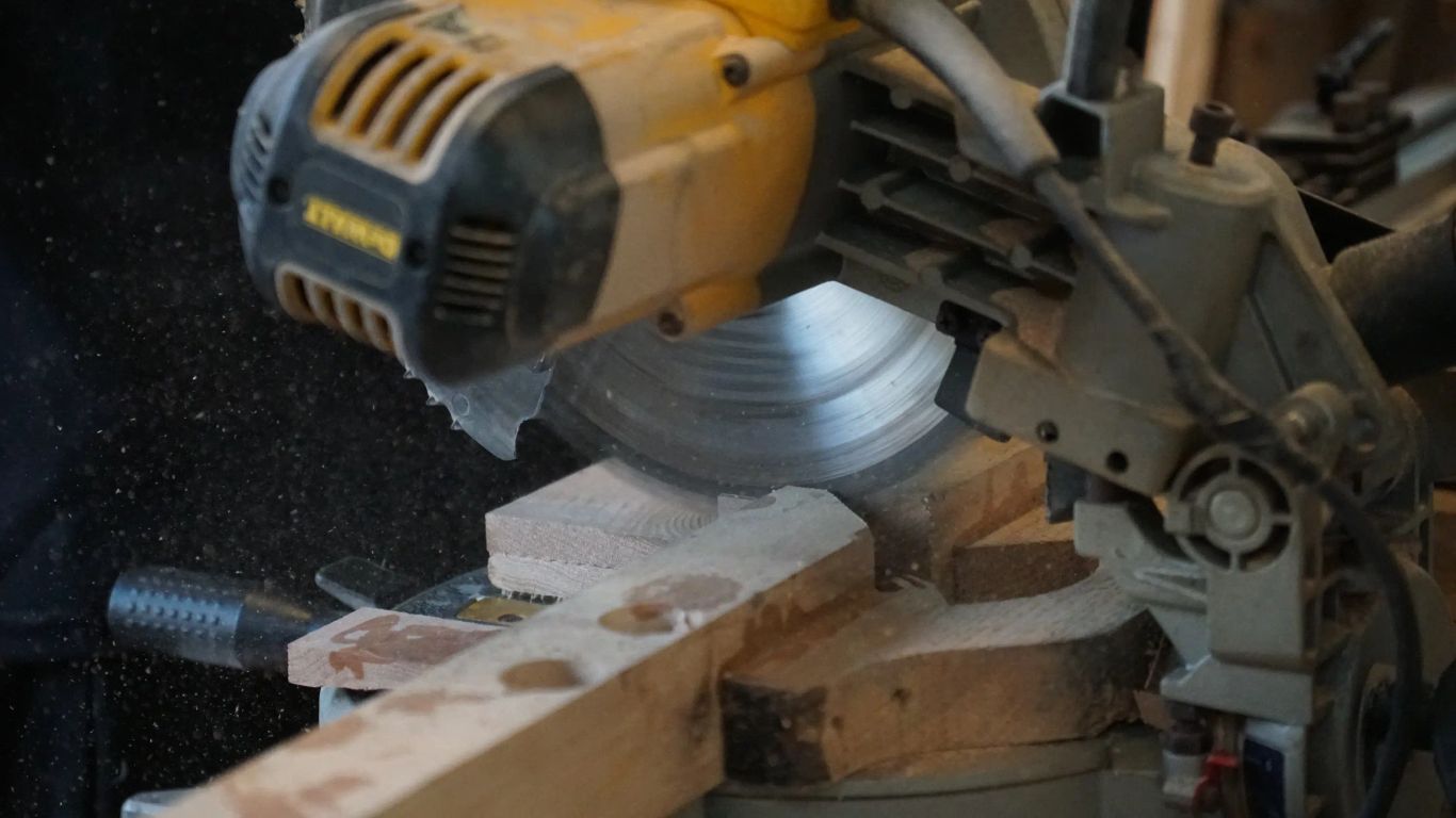 A miter saw cuts through pieces of wood, creating sawdust.