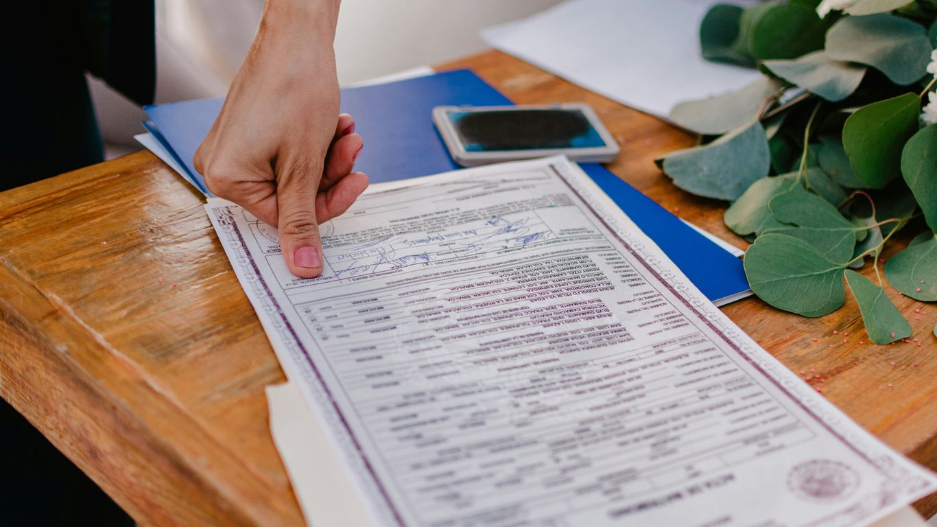 Person pointing at a marriage certificate on a wooden table.