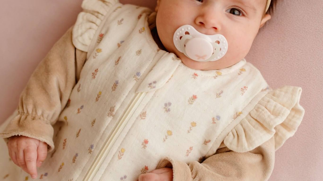 A baby wearing a floral sleep sack and a white bow.