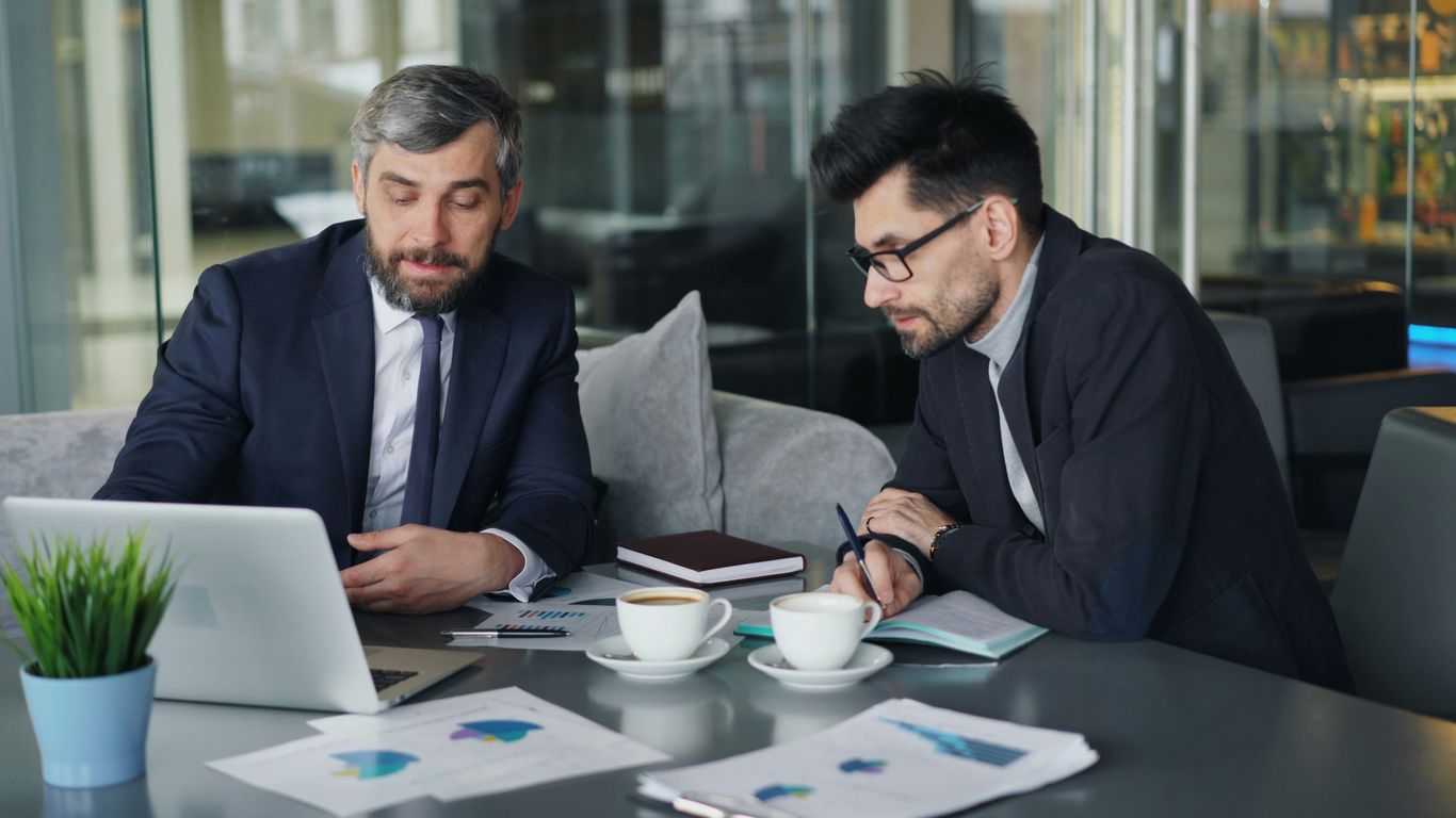 two men sitting at a table working on a laptop