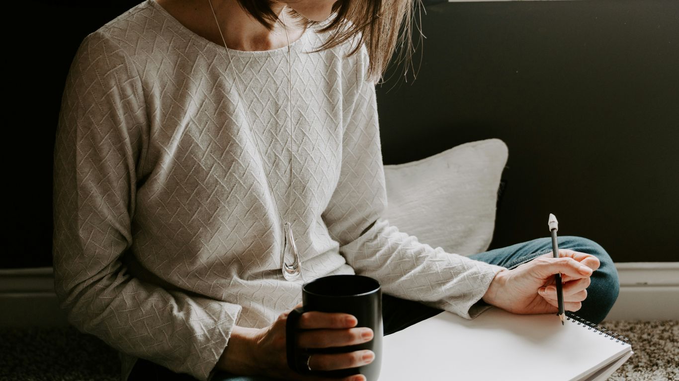 Woman writing in notebook with coffee cup