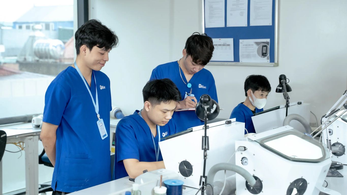 People in blue scrubs working with dental equipment in a lab.