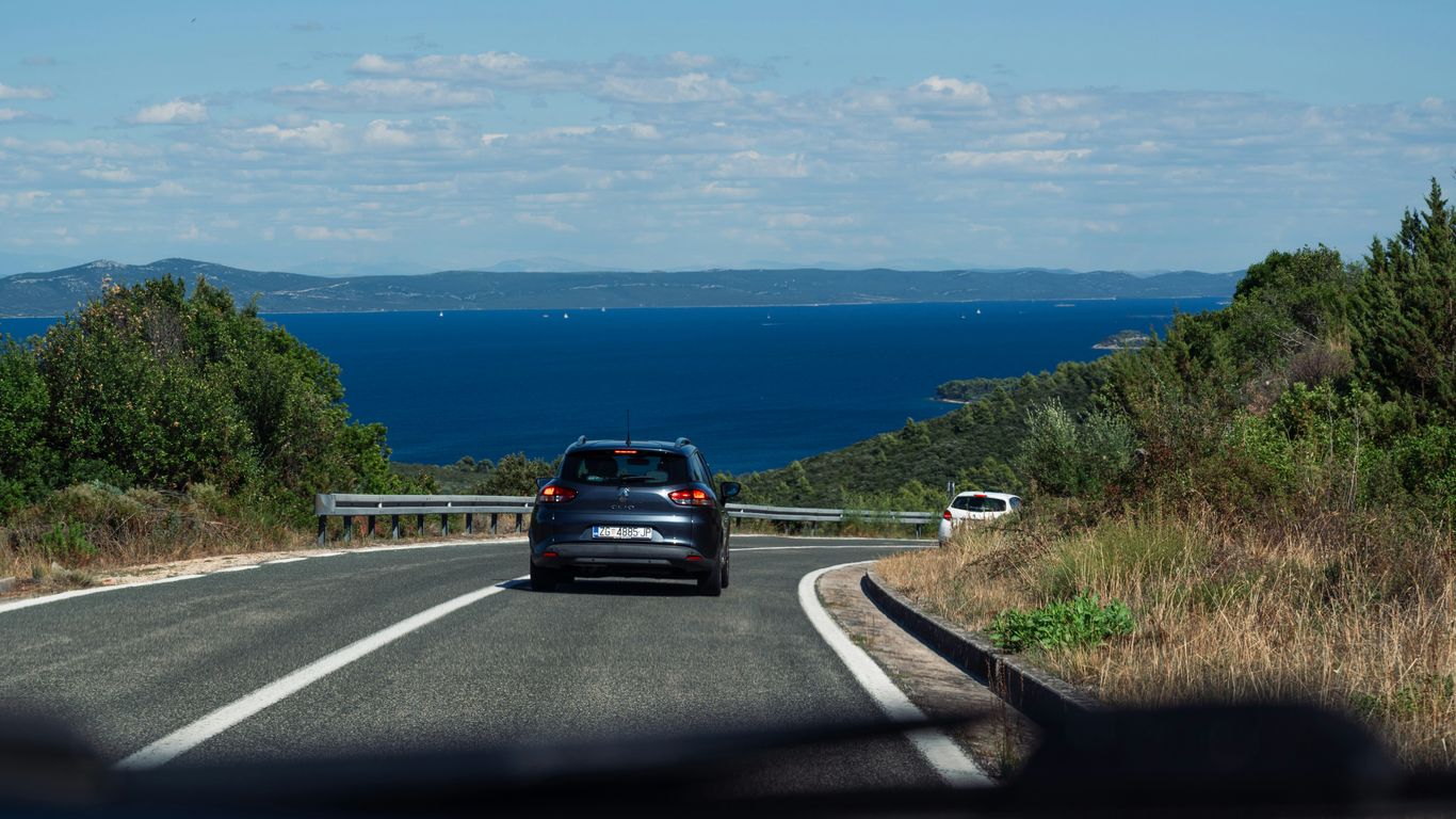 Car driving on a coastal road towards the ocean.