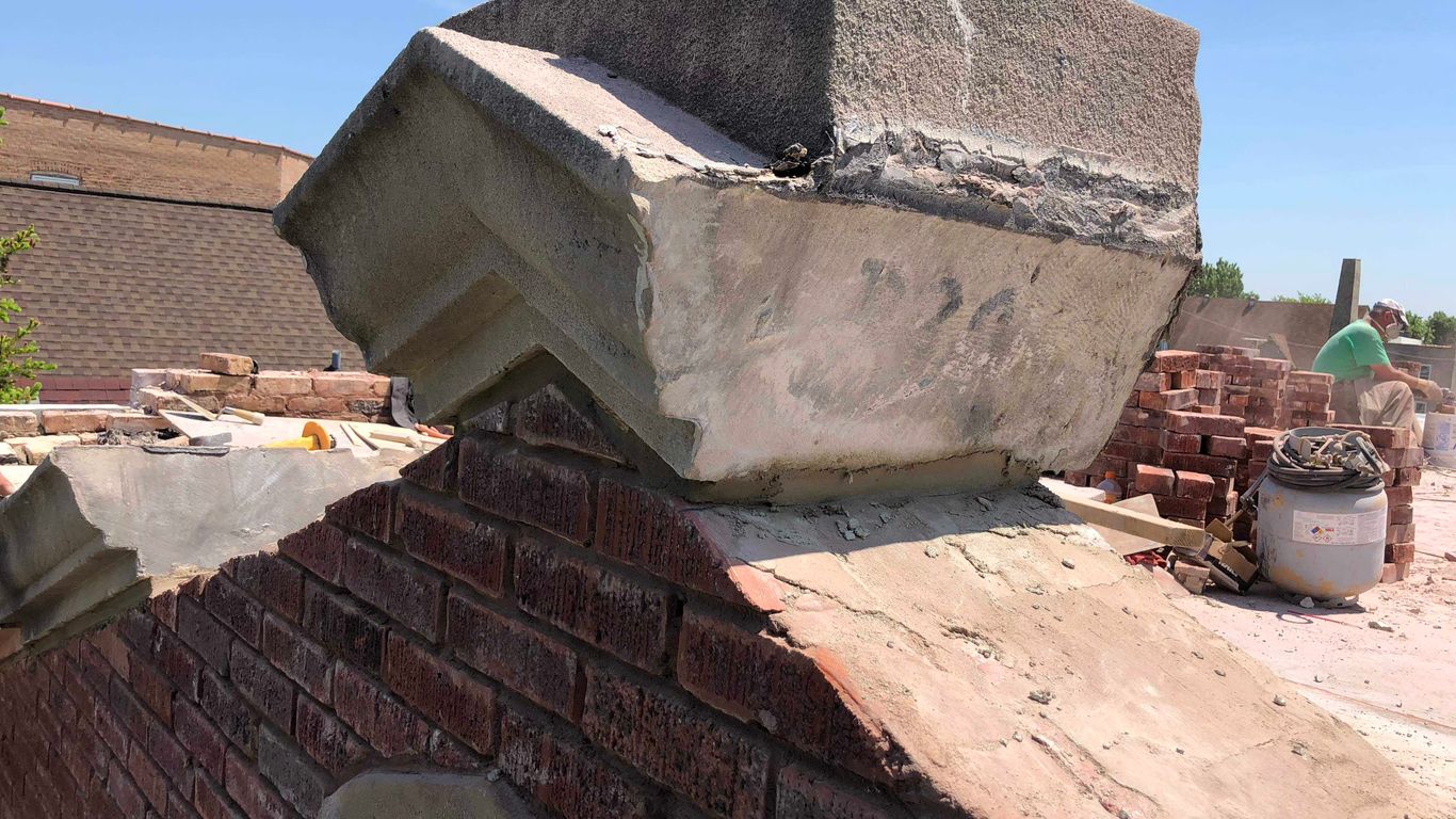 Construction workers repairing a brick chimney on a sunny day.