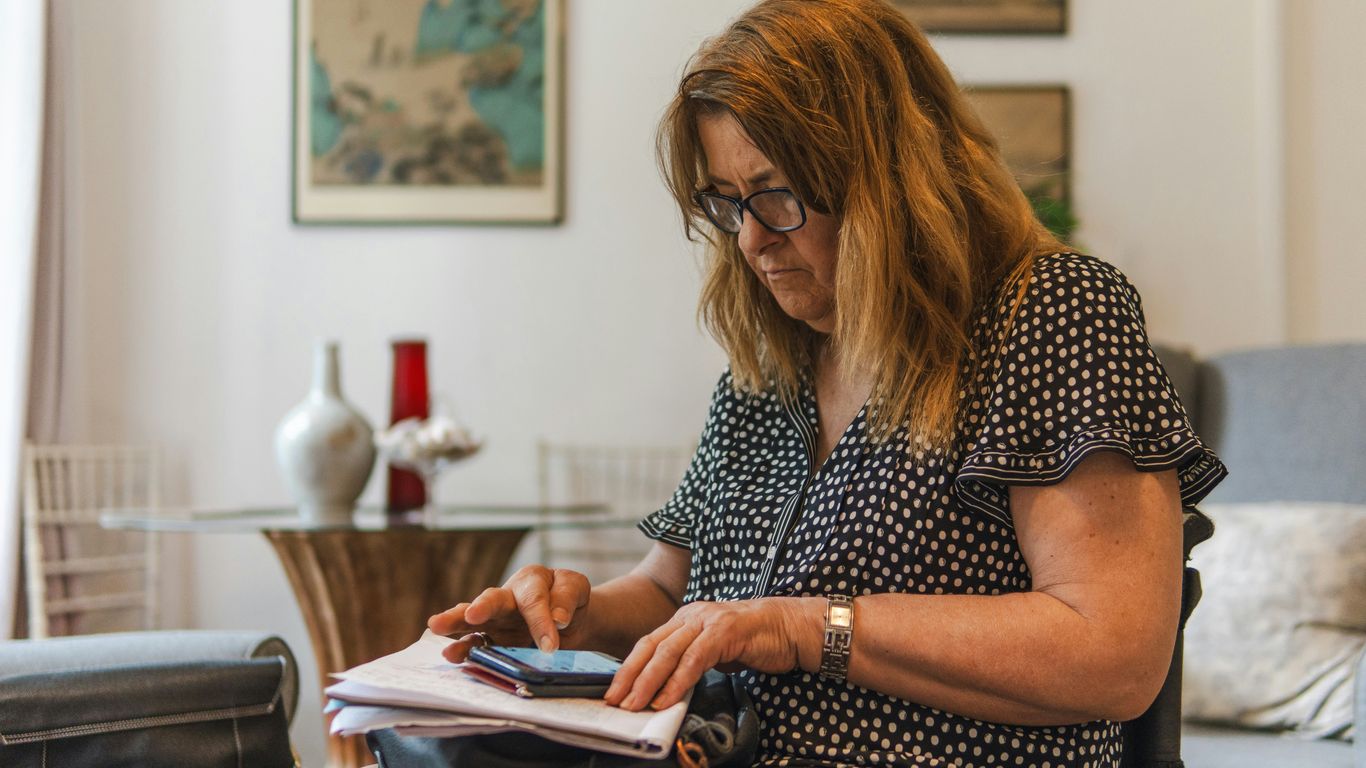 Woman looking at phone while writing on paper