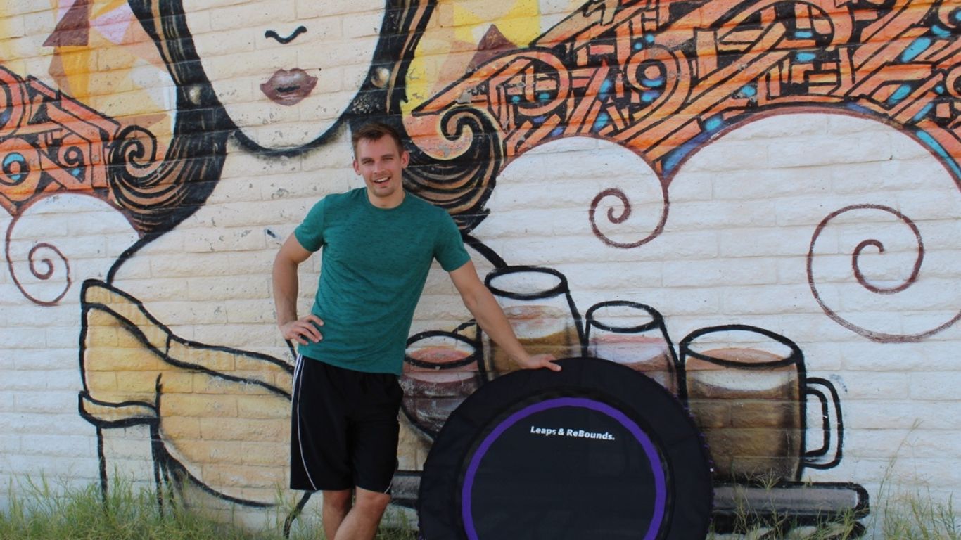 Person standing by trampoline, colorful mural with woman's face.