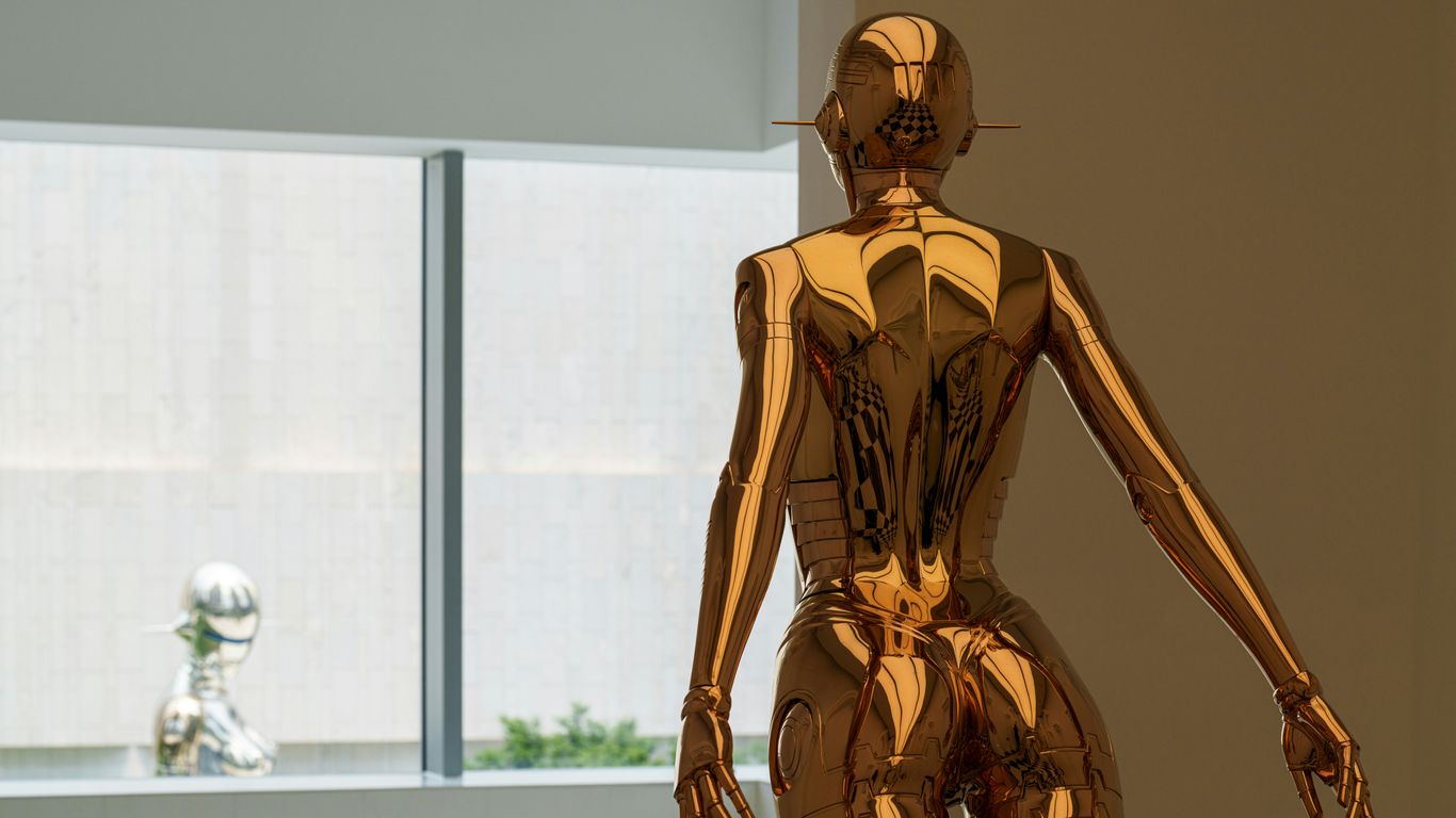 A golden statue stands near a window.