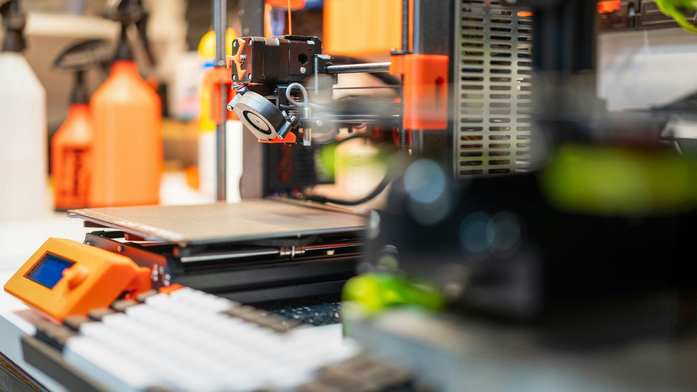 3D printer with orange accents on workbench.