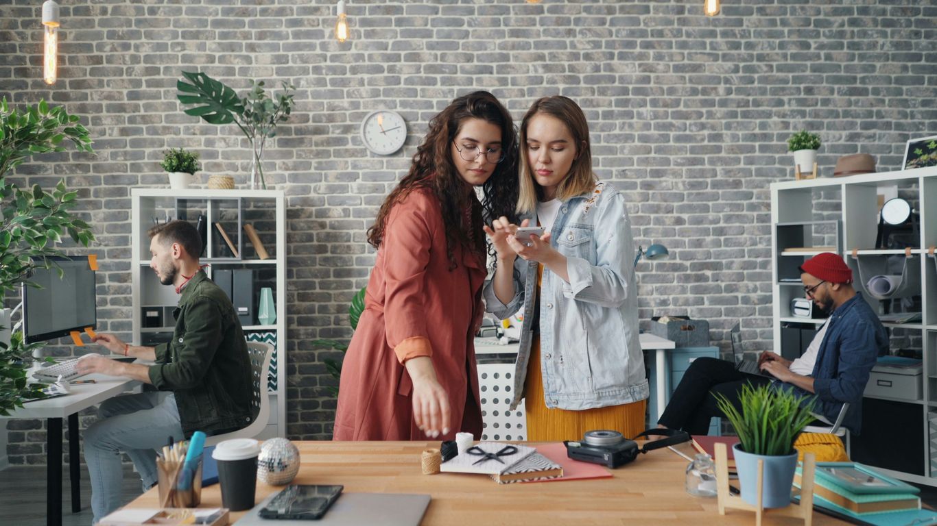 two women looking at a cell phone in an office