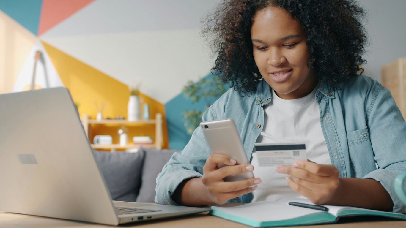 Teenager using phone and credit card for online shopping.