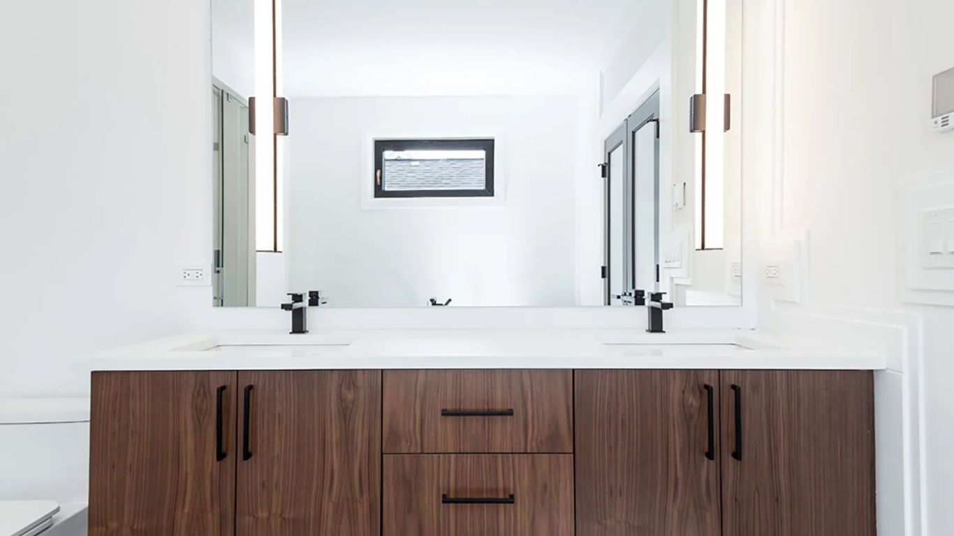 Modern bathroom with double vanity, sleek lighting, and wood cabinets.