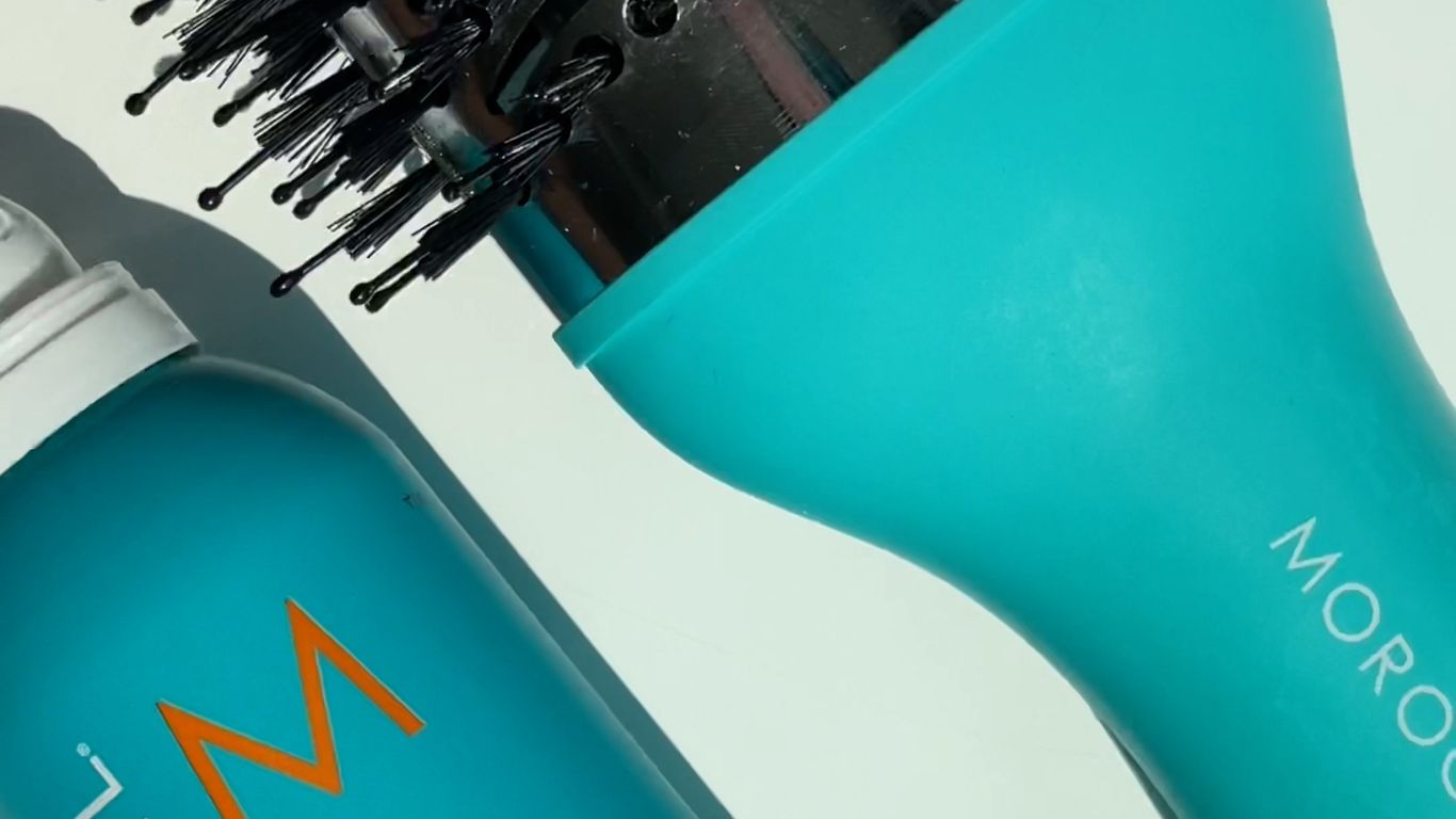 Hairbrush and Moroccanoil hair product on a white background.