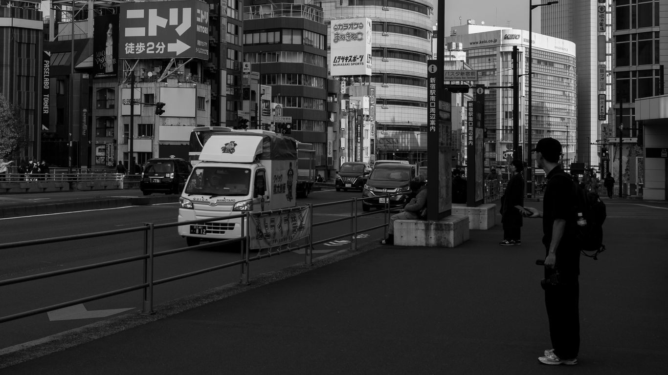 A man stands on a street with buildings and traffic.