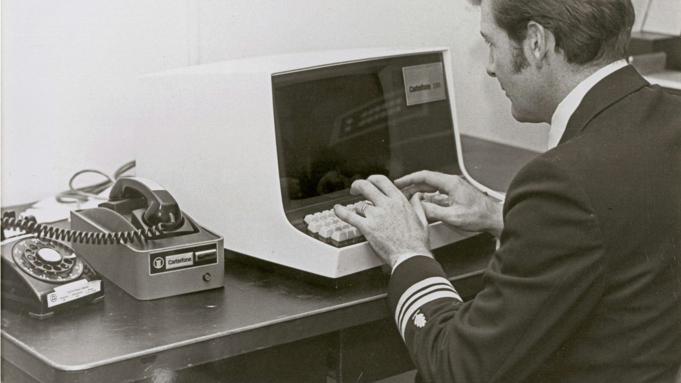 Man in uniform types on vintage computer terminal.