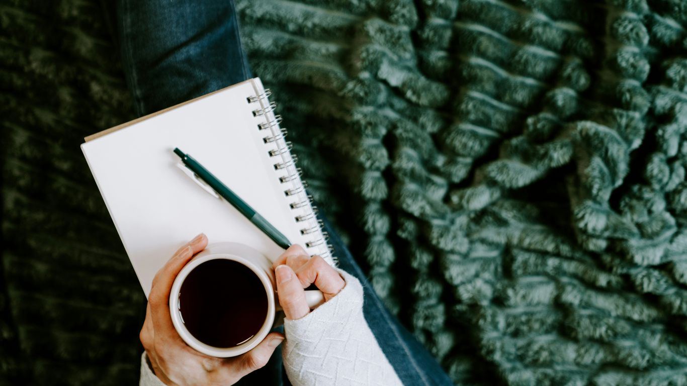 Person holding coffee cup next to notebook and pen