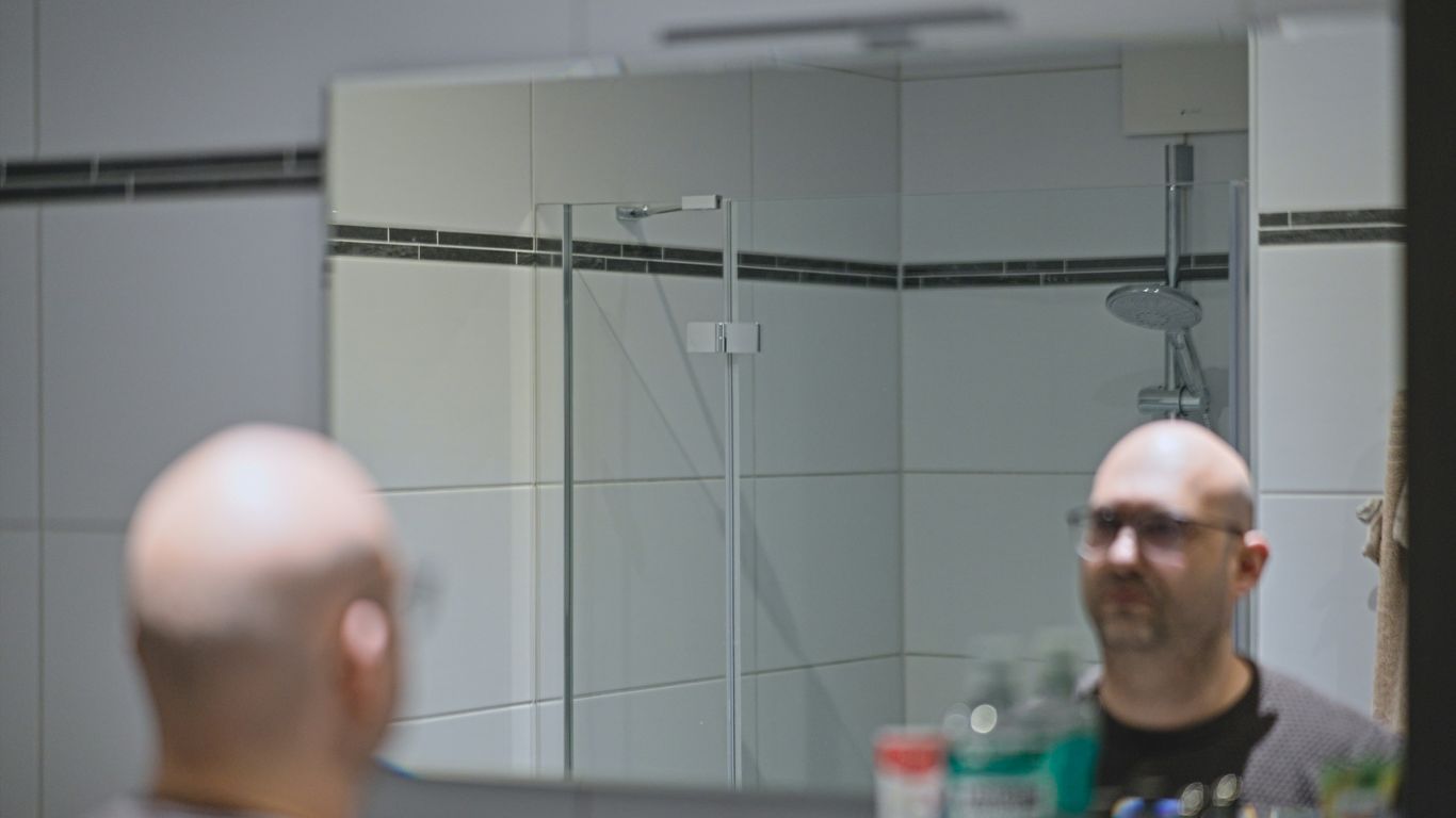 Bald man with glasses looking in bathroom mirror