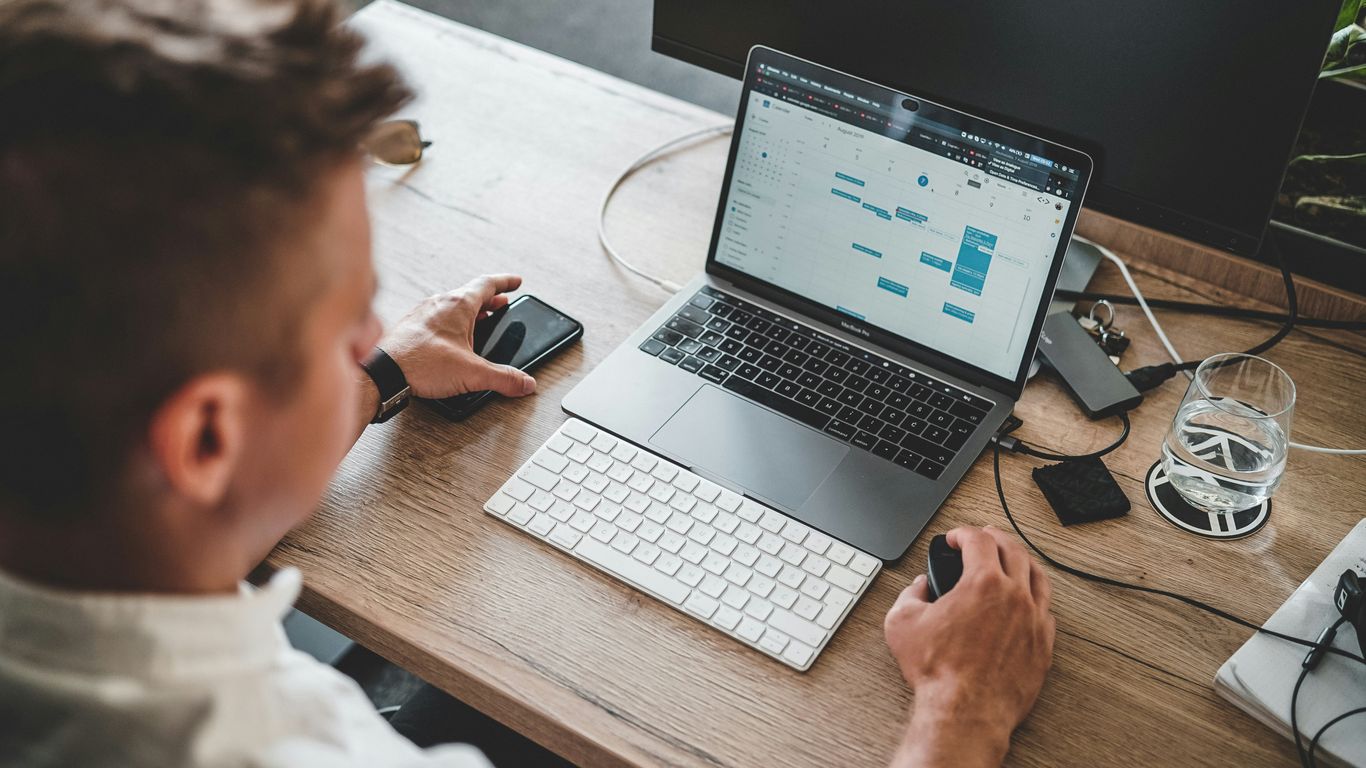 man holding mouse and iPhone while using Macbook Pro