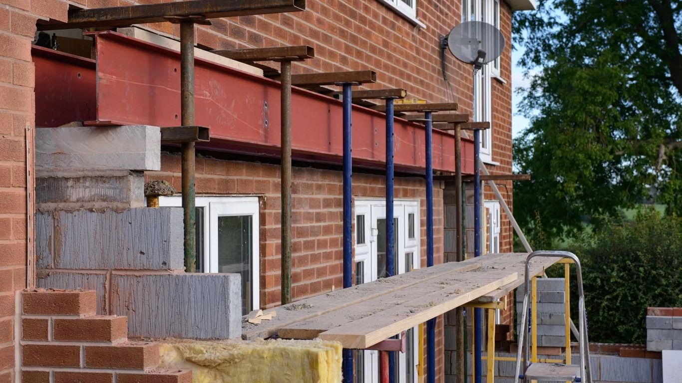 Construction site with scaffolding and steel beams supporting a brick wall.