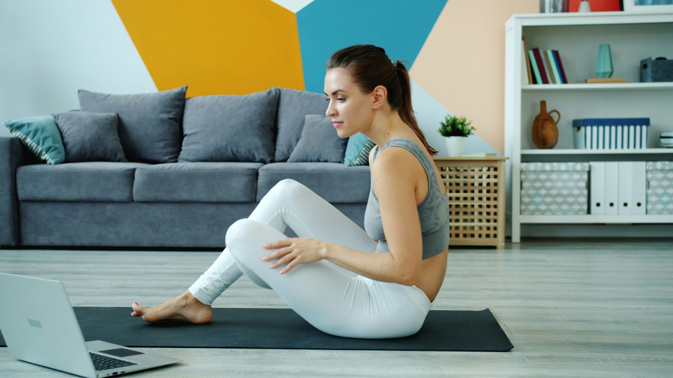 Woman exercising on yoga mat watching laptop