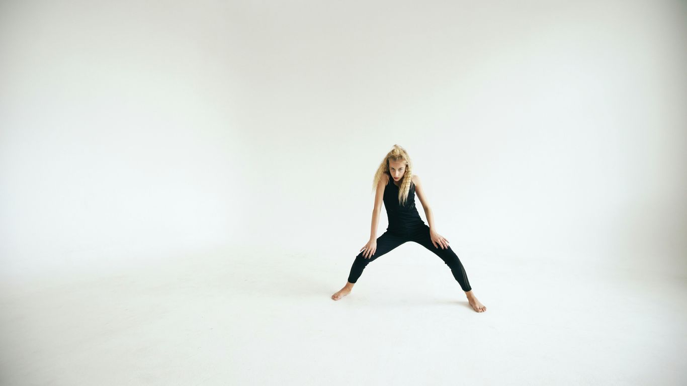 A woman in a black jumpsuit performs a dance move.
