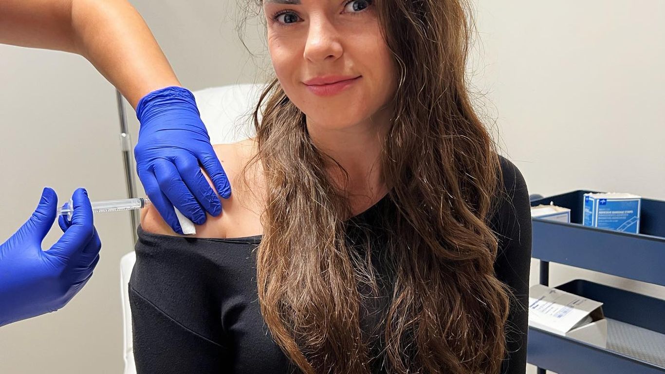 A person receives an injection in the shoulder from a gloved hand.