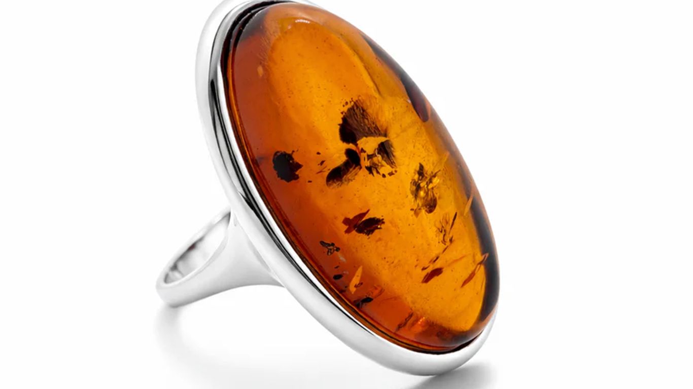A silver ring with a large oval amber stone containing inclusions.