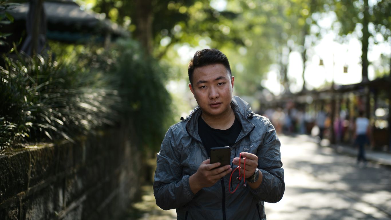 A man holding a smartphone outdoors on a sunny day.