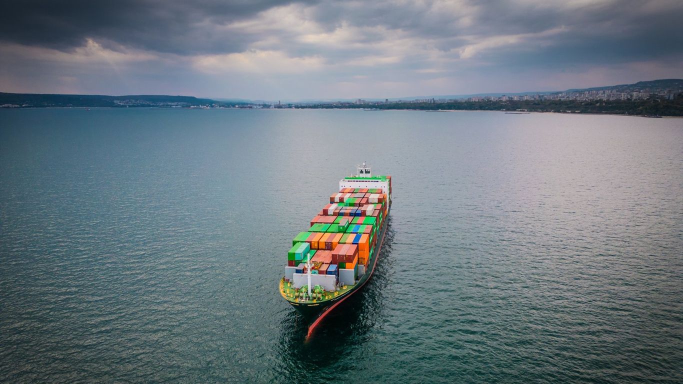 A large cargo ship filled with colorful containers sails on the sea.