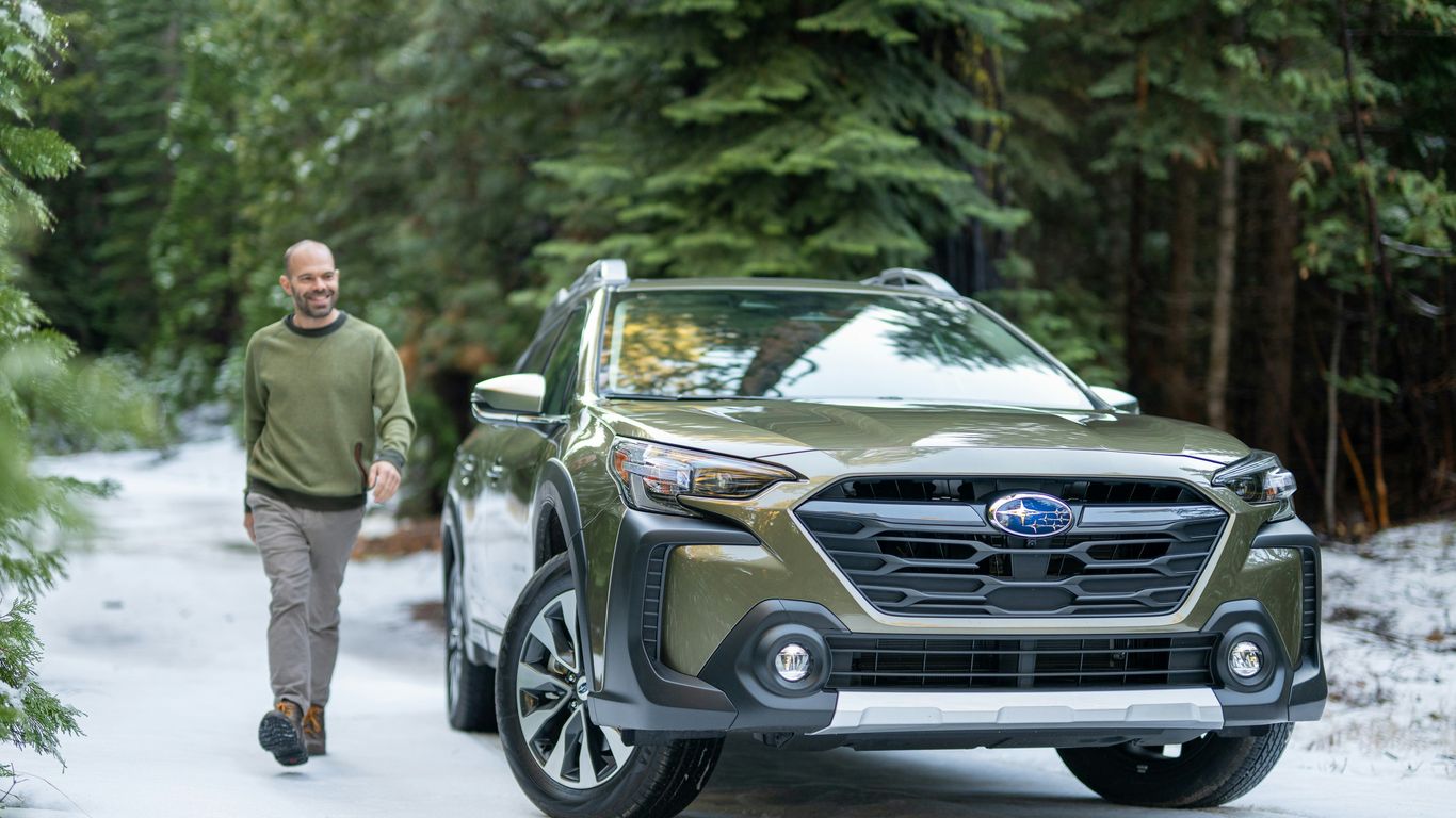 A man walking down a snow covered road next to a car