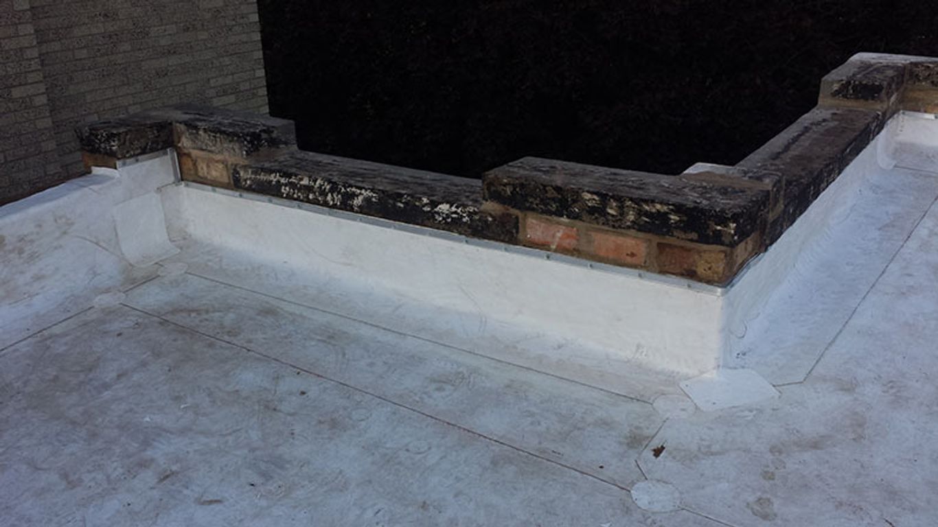 A flat roof with a brick parapet wall and white waterproofing membrane.