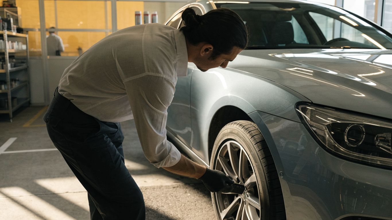 Technician checking tire tread beside a parked luxury sedan