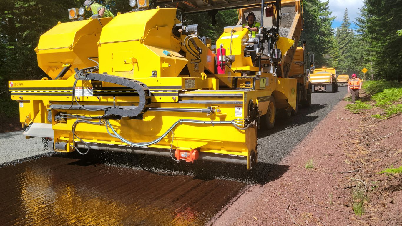 A yellow truck driving down a road next to a forest