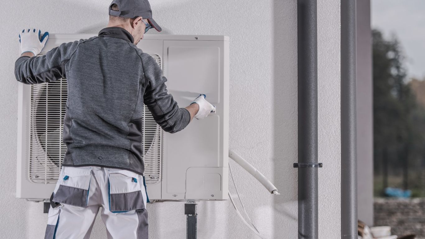 Technician installing an outdoor air conditioning unit on a wall.