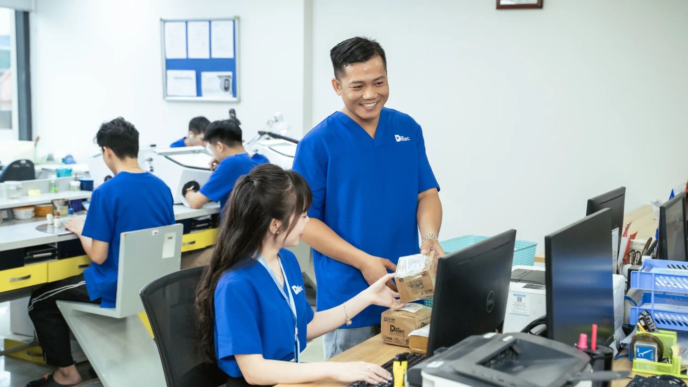People in blue uniforms working in a dental laboratory with computers.