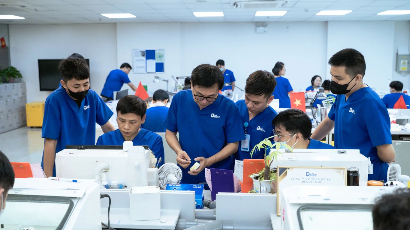 People in blue scrubs working in a dental lab with equipment.