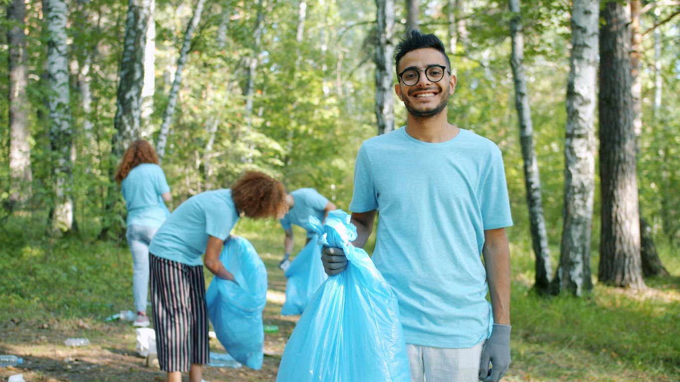 Volunteers cleaning up a forest with blue trash bags.