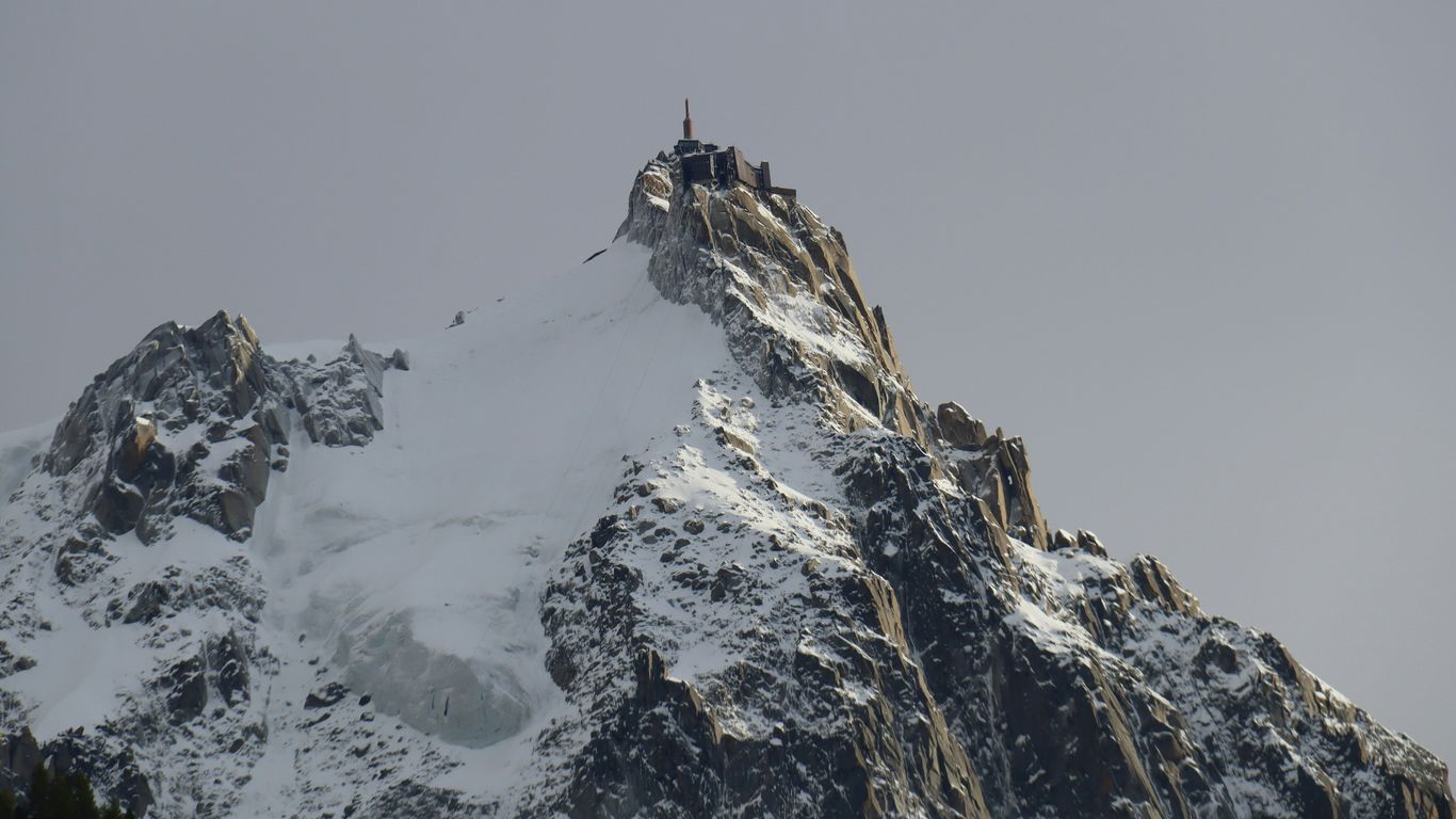 Snow-covered mountain peak with a small structure on top.