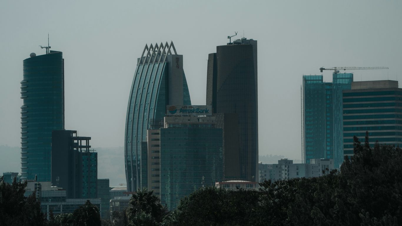 Modern skyscrapers rise above city trees on a hazy day.