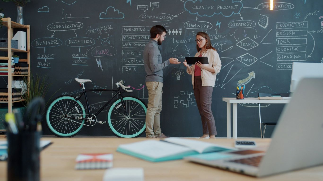 Two people discuss a plan on a chalkboard wall.