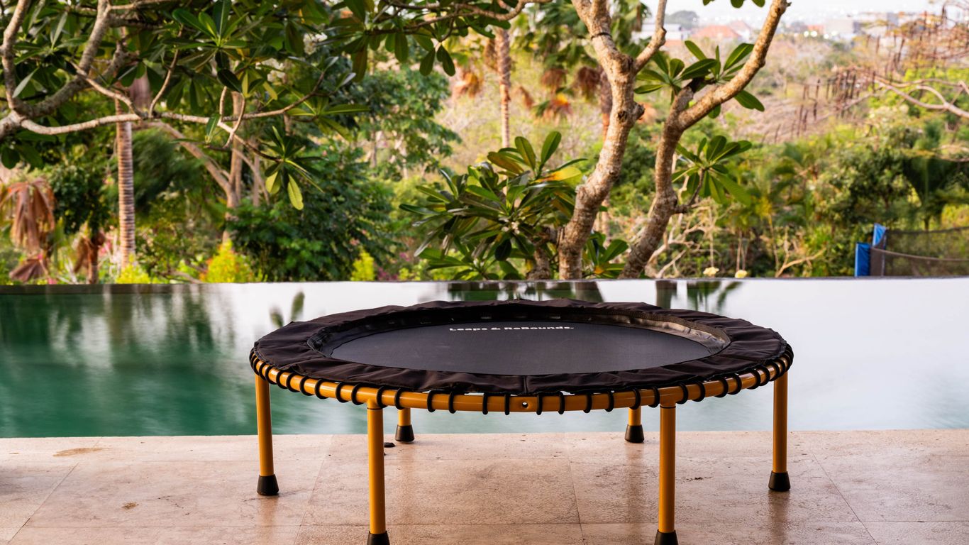 Small trampoline on patio, overlooking pool and lush greenery.